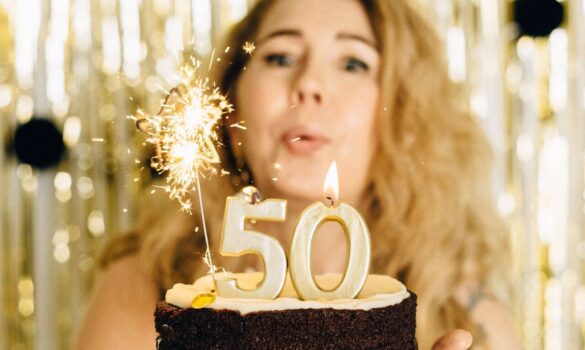 Kobieta dmuchająca w świeczki na torcie Artykuł opisuje pomysły na prezent na 50 urodziny dla kobiety.